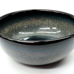 May include: A black ceramic bowl with a speckled, blue and gray glaze. The bowl has a rounded shape and a wide rim.