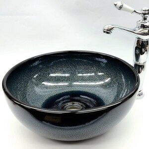 May include: A dark blue ceramic vessel sink with a chrome faucet. The sink has a textured, speckled finish and a round shape.
