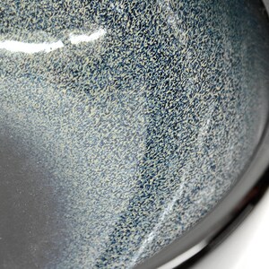 May include: A black ceramic bowl with a speckled blue and white glaze. The bowl has a rounded shape and a smooth, glossy finish.