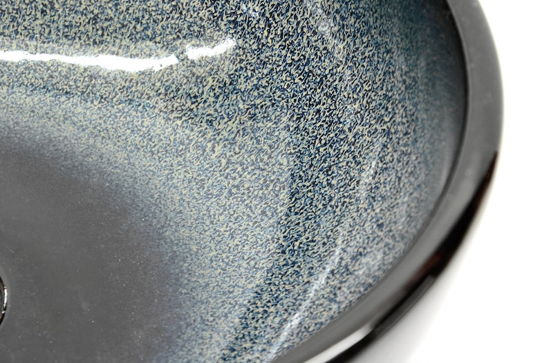 May include: A black ceramic bowl with a speckled blue and white glaze. The bowl has a rounded shape and a smooth, glossy finish.