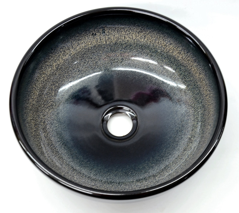 May include: A black ceramic vessel sink with a white speckled glaze. The sink has a round shape and a single drain hole in the center.