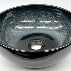 May include: A round, black ceramic vessel sink with a speckled, blue glaze. The sink has a single drain hole in the center.