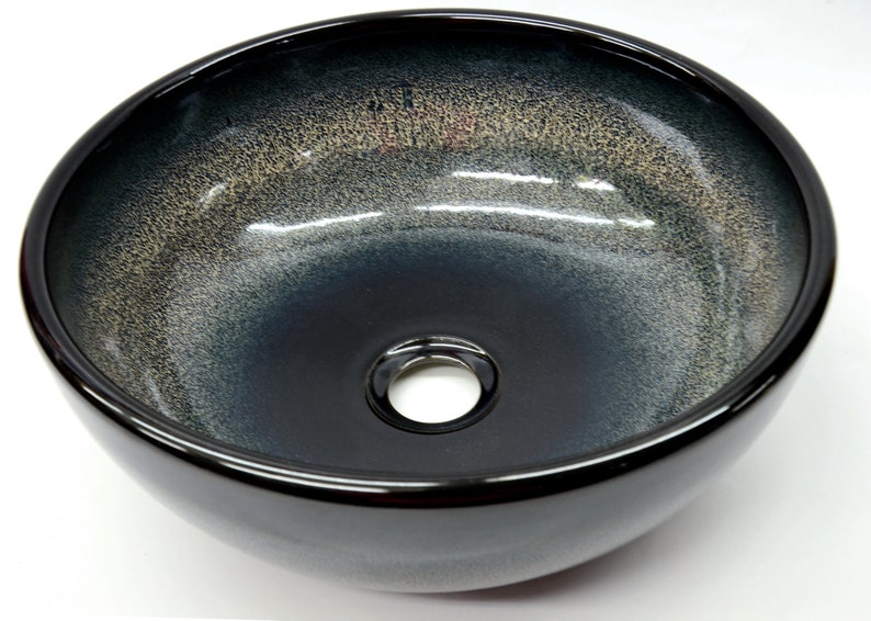 May include: A round, black ceramic vessel sink with a subtle gradient of gray and gold. The sink has a single drain hole in the center.