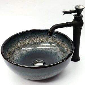 May include: A black ceramic vessel sink with a black faucet featuring a crystal knob. The sink has a speckled, dark gray and light gray glaze.