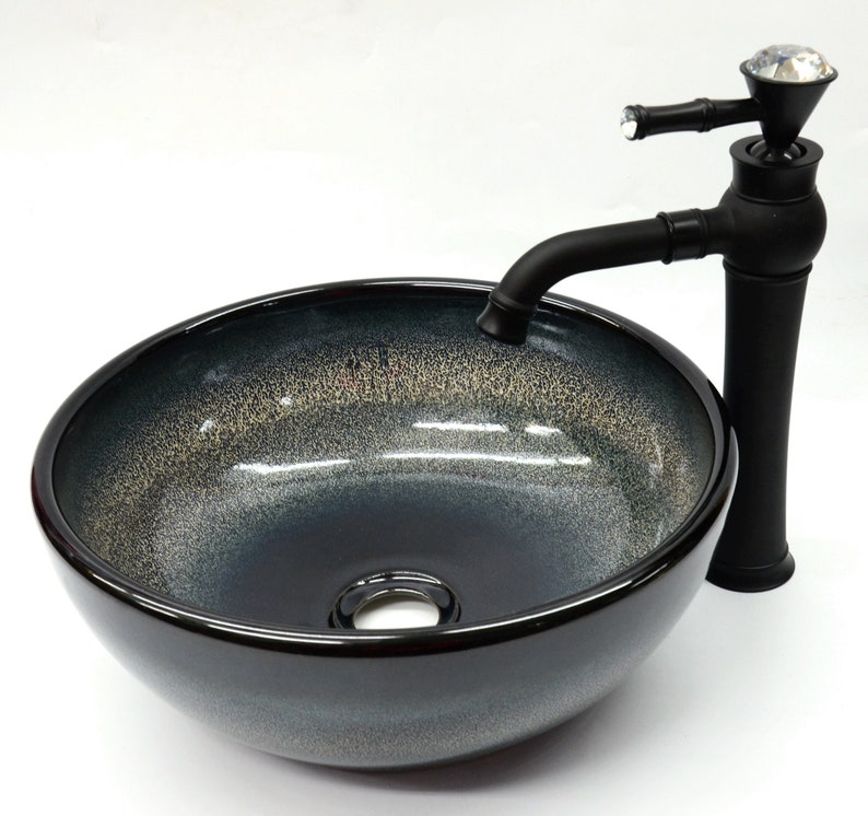 May include: A black ceramic vessel sink with a black faucet featuring a crystal knob. The sink has a speckled, dark gray and light gray glaze.