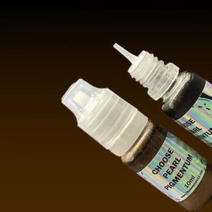 May include: Two small plastic squeeze bottles containing dark bronze liquid pigment. Each bottle features a clear nozzle cap and a holographic label with the text CHOOSE PEARL PIGMENTUM 10ml and the website address chooseyours11.com printed clearly.
