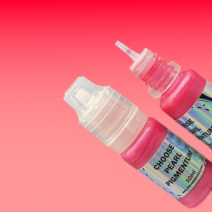 May include: Two small plastic squeeze bottles filled with vibrant pink pearl pigment. Each bottle features a clear cap and a holographic label with the text CHOOSE PEARL PIGMENTUM 10ml and the website address Chooseyours11.com printed clearly.
