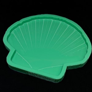May include: A green silicone mold shaped like a seashell. The mold has a detailed design of a seashell with ridges and lines.