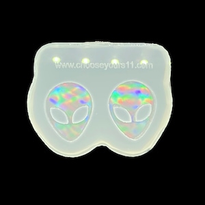 Può includere: Uno stampo in silicone trasparente con due disegni di teste aliene con dettagli iridescenti e color arcobaleno. Lo stampo ha una forma arrotondata con il testo "www.chooseyours11.com" stampato in alto. Lo sfondo è nero.