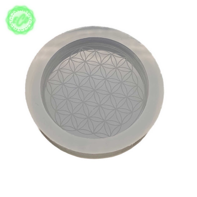 May include: A white silicone mold with a raised flower of life design. The mold is round and has a raised edge.