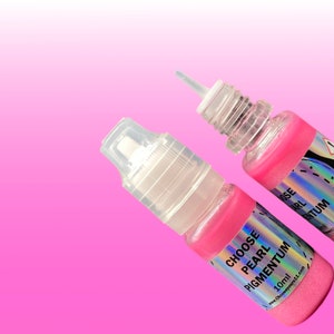 May include: Two small plastic squeeze bottles containing pink pearl pigmentum. Each bottle features a clear cap, a narrow nozzle, and a holographic label with the text CHOOSE PEARL PIGMENTUM 10ml and the website address printed on it.