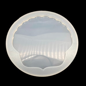 May include: A clear, flexible silicone mold in the shape of a seashell. The mold has a scalloped edge and a smooth interior, designed for crafting resin art or other DIY projects. The mold is circular and sits against a black background.