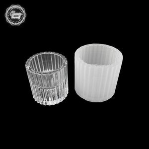 May include: Two cylindrical containers. One is clear glass with vertical ridged detailing. The other is a white, opaque, cylindrical mold with similar vertical ridged detailing. The containers are on a black background. The image includes a logo in the top left corner.