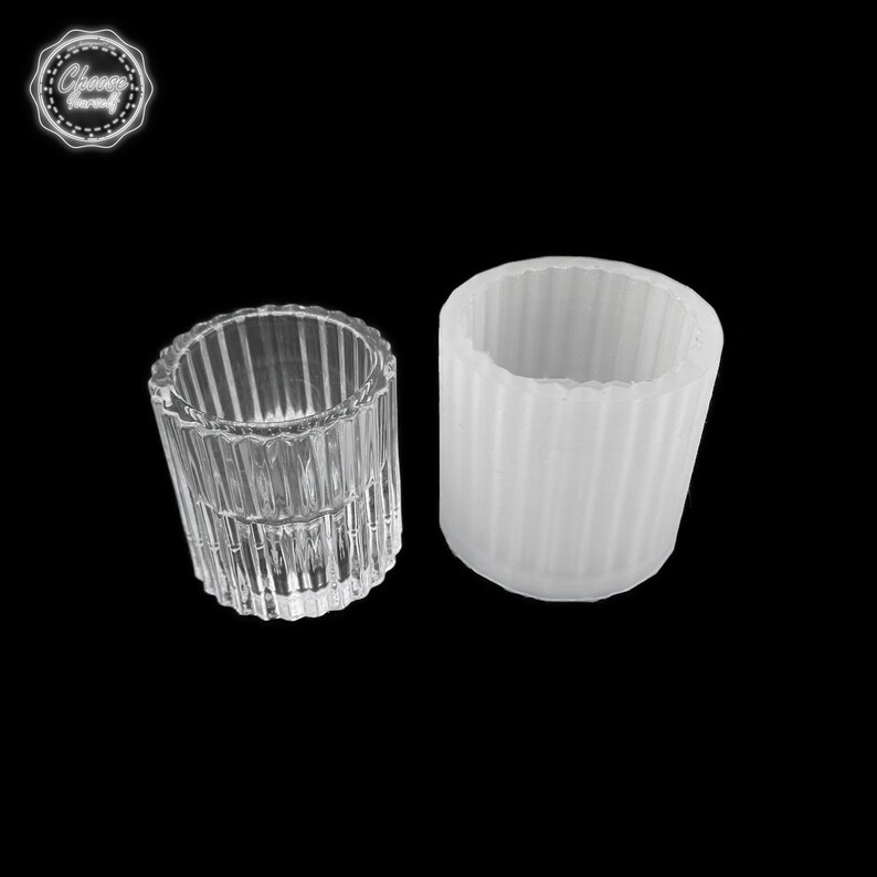 May include: Two cylindrical containers. One is clear glass with vertical ridged detailing. The other is a white, opaque, cylindrical mold with similar vertical ridged detailing. The containers are on a black background. The image includes a logo in the top left corner.