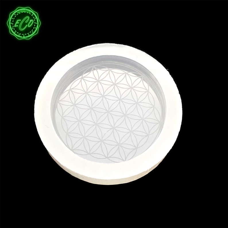 May include: White silicone mold with a raised flower of life design. The mold is round and has a smooth surface.