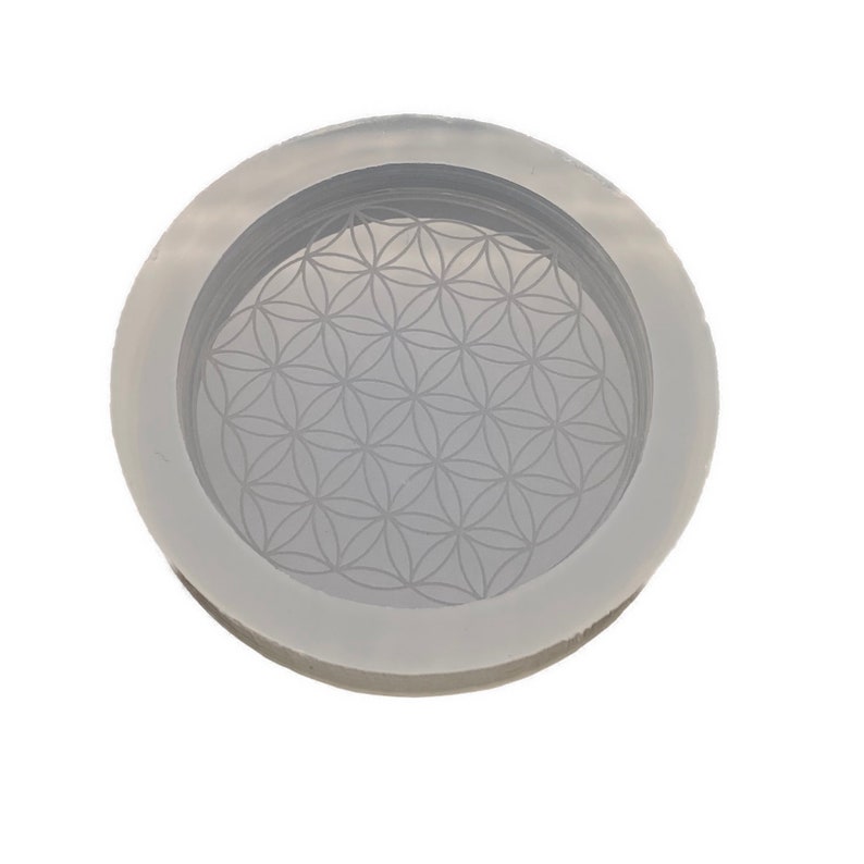 May include: A white silicone mold with a raised flower of life design. The mold is round and has a raised rim.