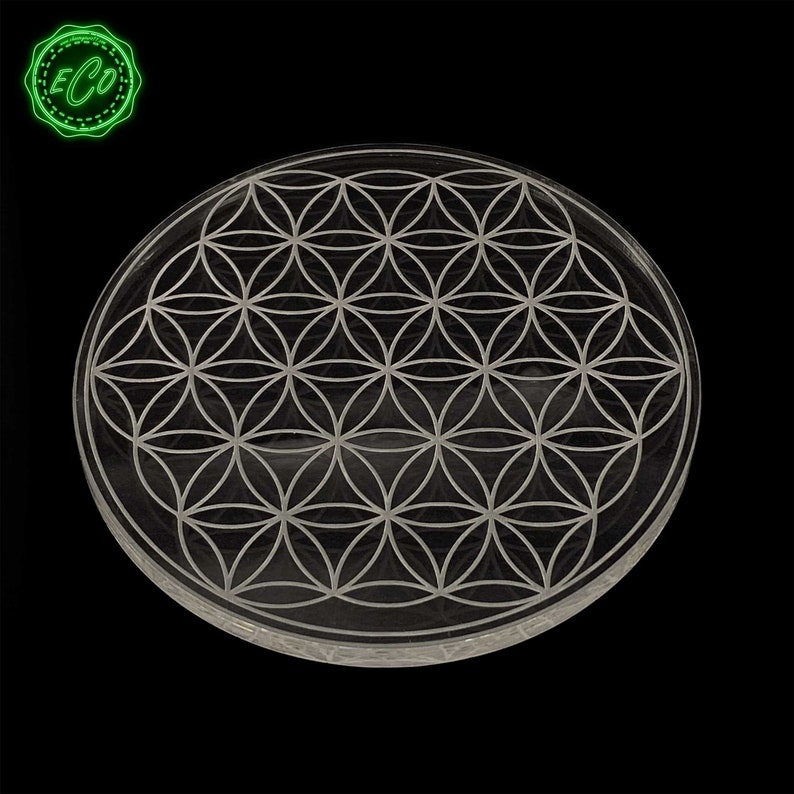 May include: A clear glass coaster with a white flower of life design etched into the surface.