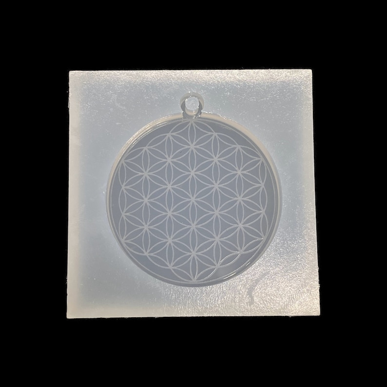 May include: A clear silicone mold for making resin jewelry. The mold is shaped like a circle and features a raised design of a flower of life pattern.