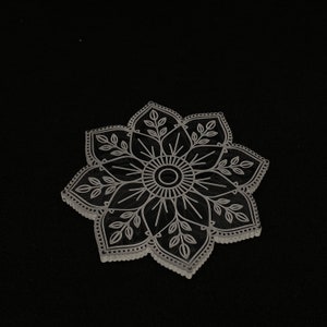 May include: A white, laser-cut mandala design with intricate details, resembling a flower with multiple petals and leaves.
