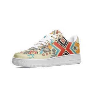 May include: A cream-coloured trainer with a white sole and laces. The shoe features a colourful geometric pattern in red, orange, blue, and black. The design includes shapes like diamonds, squares, and triangles.