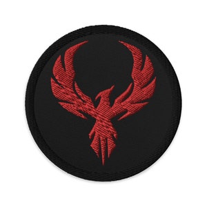 May include: Circular black embroidered patch with a red phoenix emblem. The phoenix is shown with detailed wings and a stylized design. The patch has a black border and is suitable for clothing or accessories.