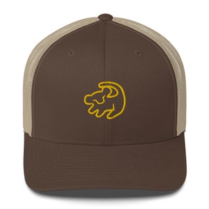 Puede incluir: Una gorra de camionero marrón y beige con un símbolo del rey león bordado en amarillo en la parte delantera.