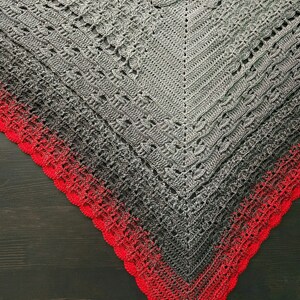 Puede incluir: Un chal de ganchillo gris y rojo con un borde festoneado. El chal está hecho con un hilo degradado que pasa de gris a rojo.