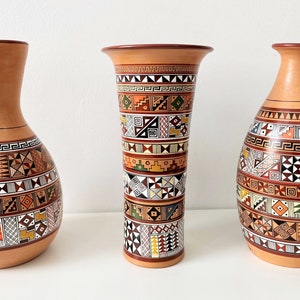 May include: Three ceramic vases with geometric patterns in shades of brown, orange, yellow, green, black, and white. The vases are all different shapes and sizes.