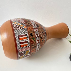 May include: A terracotta vase with a geometric pattern in shades of brown, orange, white, and green. The vase is hand-painted with a traditional design.