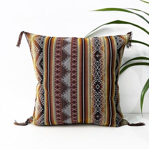 May include: A brown, beige, and white striped throw pillow with a geometric pattern. The pillow has tassels on each corner.