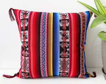 May include: Red, blue, and yellow striped throw pillow with a geometric pattern and tassels. The pillow is made of woven fabric.