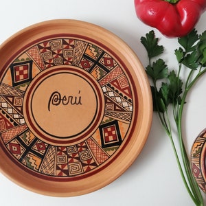 May include: A terracotta plate with a geometric design in shades of red, brown, black, and yellow. The plate has the word "Per&uacute;" written in cursive in the center.