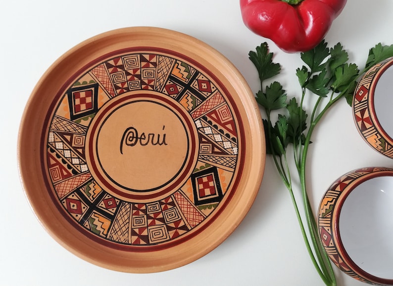 May include: A terracotta plate with a geometric design in shades of red, brown, black, and yellow. The plate has the word "Per&uacute;" written in cursive in the center.