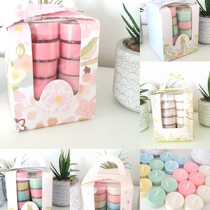 Könnte beinhalten: Mehrere Schachteln mit Teelichtkerzen in verschiedenen Pastellfarben. Die Schachteln sind mit Blumen- und Hasenmotiven verziert. Jede Schachtel hat ein klares Fenster zur Präsentation der Kerzen. Die Kerzen sind rosa, blau, grün und weiß.