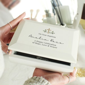May include: White wooden keepsake box with a gold cross and green leaves design. The box has the text "On Your Baptism Amelia Rose A Happy Celebration of Hope, Love & Prayer" on the lid.
