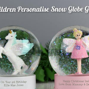 May include: Two snow globes with personalized text. One features a white unicorn with blue wings, the other a fairy in a pink dress. Both globes have glitter and sit on white and pink bases. The text reads "Children Personalise Snow Globe Gifts".