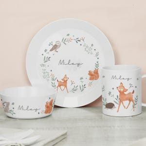 Puede incluir: Un juego de vajilla blanco para niños con plato, cuenco y taza. Cada pieza está decorada con animales del bosque, como un ciervo, una ardilla y un búho, y el nombre "Miley". El conjunto tiene un diseño caprichoso inspirado en la naturaleza.