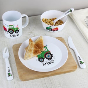Puede incluir: Un juego de vajilla infantil de plástico blanco con un diseño de tractor verde. El juego incluye un tazón, un plato, una taza, un tenedor, un cuchillo y una cuchara. El nombre "Arthur" está impreso en cada pieza.