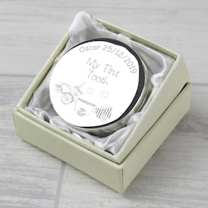 Könnte beinhalten: Eine silberne Erinnerungsbox mit einem Zugdesign und der Aufschrift "Oscar 25/12/2019 Mein erster Zahn". Die Box befindet sich in einer weißen Box mit Satin-Futter.
