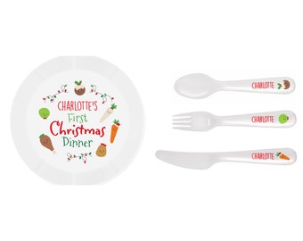 Puede incluir: Un juego de plato y cubiertos blancos para la primera cena de Navidad de un niño. El plato presenta el texto "Charlotte's First Christmas Dinner" con ilustraciones festivas de alimentos. Los cubiertos son blancos y personalizados con el nombre "Charlotte".