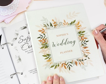 May include: A white wedding planner with a green and orange floral design. The text "SOPHIE'S Wedding PLANNER" is printed on the front.