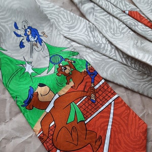 May include: A brown and orange tie with a green, orange, and white tennis court design. The tie features cartoon bears playing tennis with a blue bird in the background.