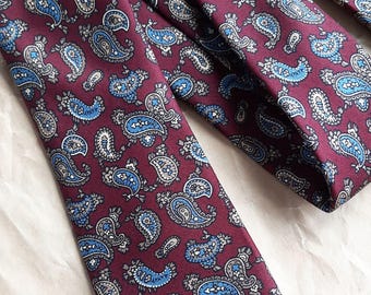 May include: Burgundy-colored neckties with a repeating paisley pattern in shades of blue and white. The ties are made of a smooth fabric and are arranged on a light-colored surface. The ties are a classic accessory.