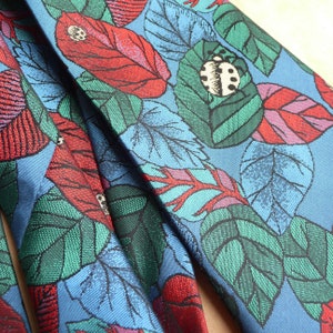 May include: A blue fabric with a repeating pattern of green leaves, red flowers, and black ladybirds.
