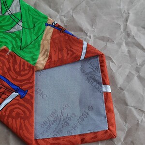 May include: A red, green, and white patterned silk tie with a blue and white design. The tie has a gray lining with the text 'Made in Italy' and '100% Silk' printed on it.