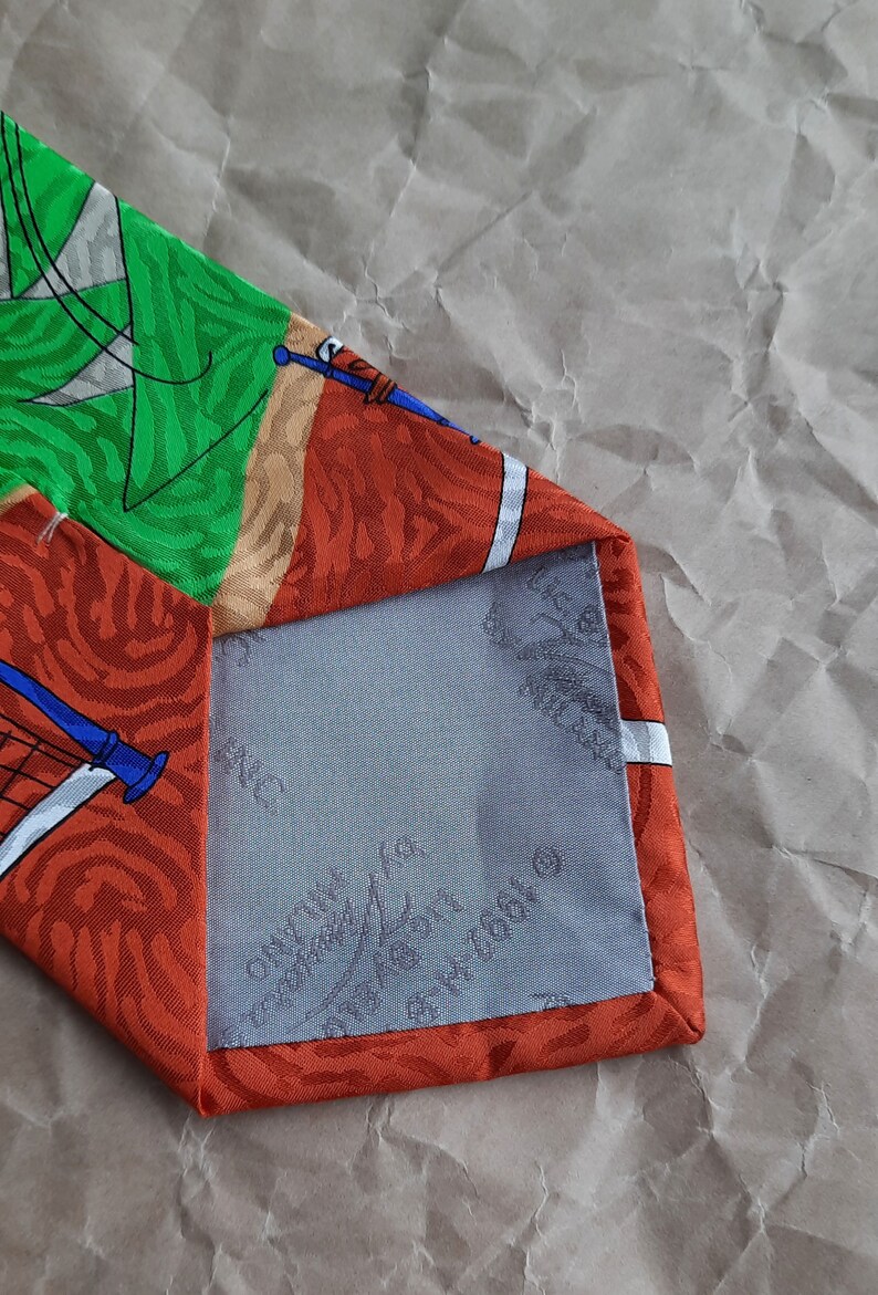 May include: A red, green, and white patterned silk tie with a blue and white design. The tie has a gray lining with the text 'Made in Italy' and '100% Silk' printed on it.