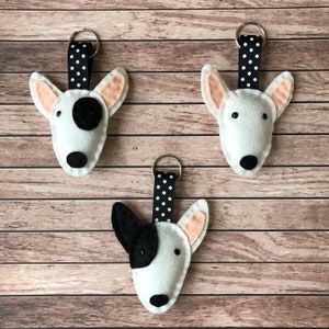 May include: Three white felt bull terrier dog keyrings with black spots. Each keyring has a black and white polka dot ribbon attached to a silver ring.