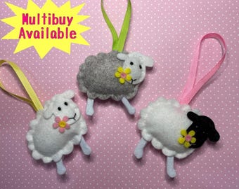 May include: Three felt sheep ornaments with a flower on each. The sheep are white, gray, and black and white. The ornaments are hanging from pink ribbon.