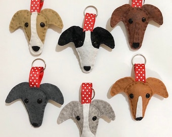 May include: Six felt greyhound dog keychains with red and white polka dot ribbon loops. The greyhounds are in various colors, including brown, black, grey, and white.