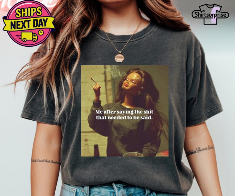 K&ouml;nnte beinhalten: Dunkelgraues T-Shirt mit einem Aufdruck einer rauchenden Frau und dem Text "Me after saying the shit that needed to be said." Das T-Shirt hat eine lockere Passform und kurze &Auml;rmel.